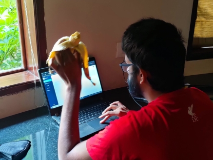 A man sitting and working on a laptop, and eating a banana