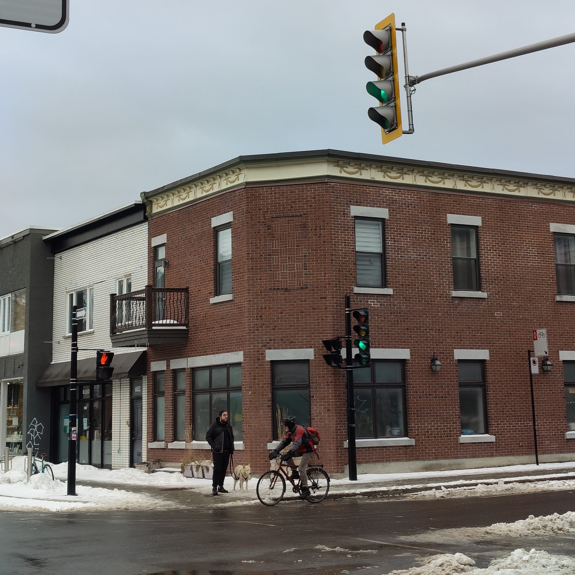 A Montreal intersection in winter that has a cyclist, and a man walking his dog